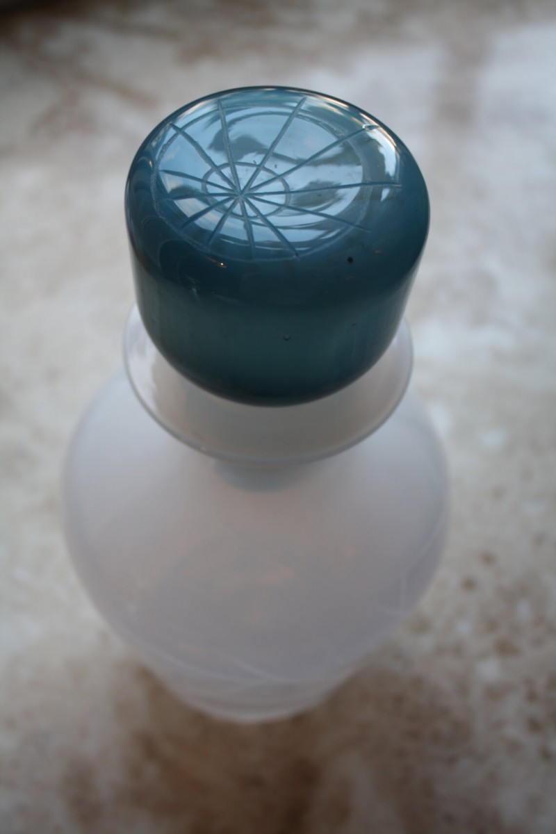 A white glass decanter with blue glass stopper viewed from above. The stopper is engraved with markings resembling the point where longitude lines meet on a globe